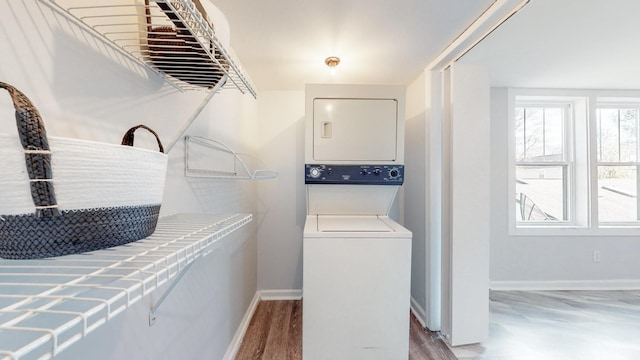 washroom with light wood-type flooring, stacked washer / drying machine, laundry area, and baseboards