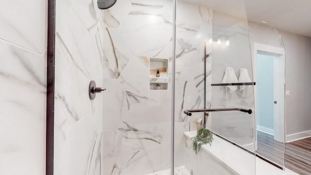 full bath with wood finished floors, a marble finish shower, and baseboards