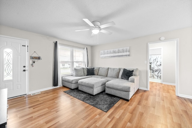 living room featuring visible vents, ceiling fan, a textured ceiling, light wood-type flooring, and baseboards