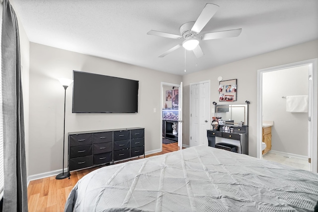 bedroom with light wood-style floors, ceiling fan, ensuite bath, and baseboards