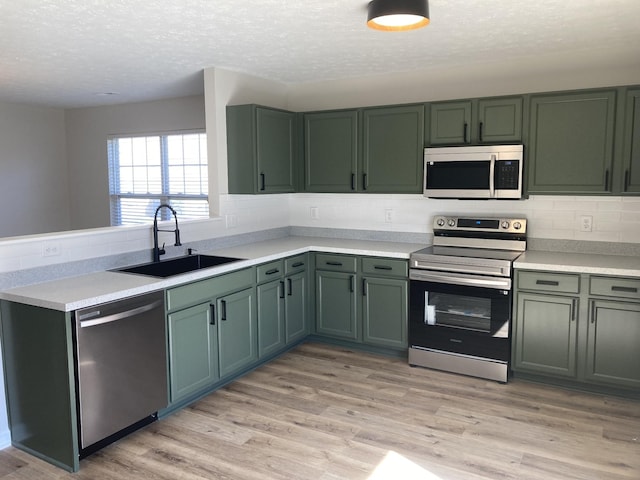 kitchen featuring green cabinetry, appliances with stainless steel finishes, light countertops, light wood-style floors, and a sink