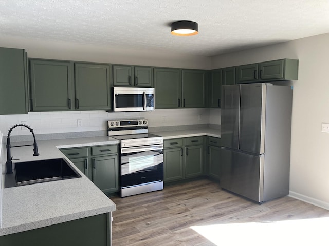 kitchen with light wood finished floors, stainless steel appliances, light countertops, green cabinets, and a sink