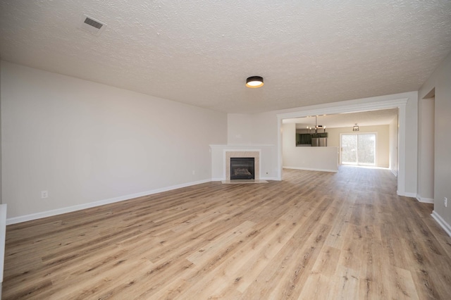 unfurnished living room with wood finished floors, visible vents, baseboards, a fireplace with flush hearth, and a textured ceiling