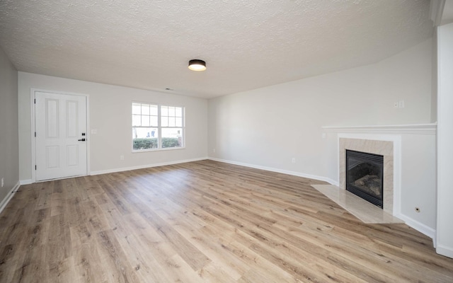 unfurnished living room featuring wood finished floors, baseboards, a high end fireplace, and a textured ceiling