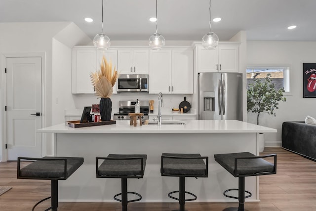 kitchen featuring a breakfast bar area, stainless steel appliances, white cabinetry, light countertops, and light wood-type flooring