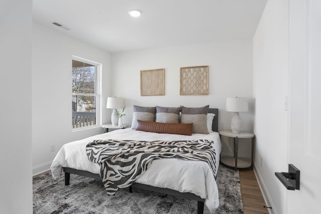 bedroom with baseboards, visible vents, and wood finished floors