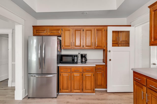 kitchen featuring light wood finished floors, black microwave, light countertops, and freestanding refrigerator