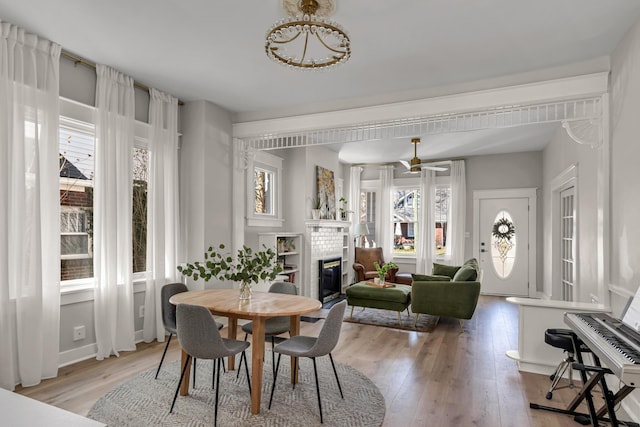 dining area featuring light wood-style floors, a brick fireplace, and a ceiling fan