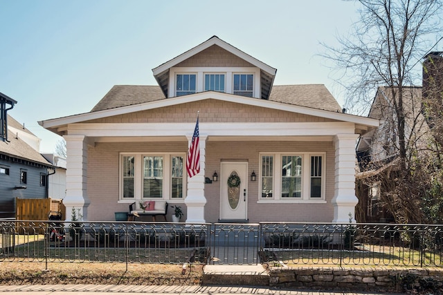 bungalow-style home featuring a porch, a fenced front yard, and brick siding