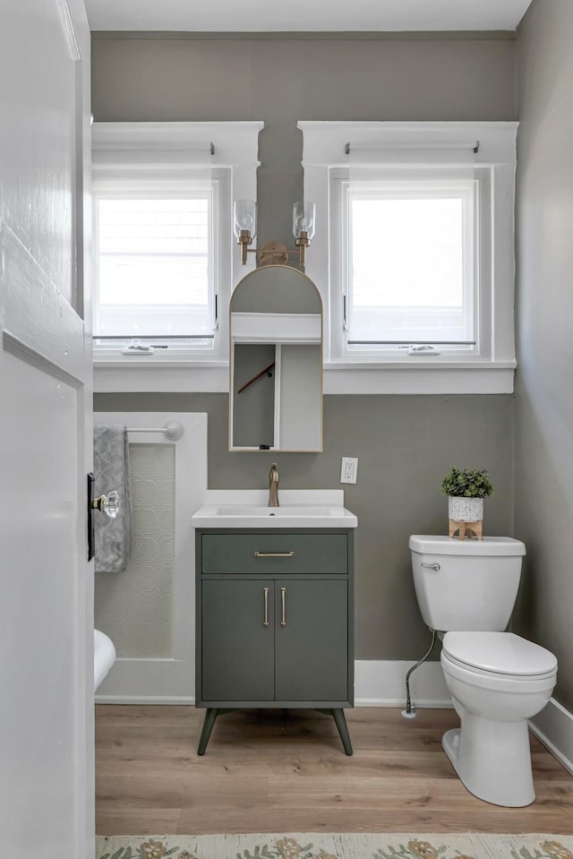 bathroom featuring toilet, baseboards, wood finished floors, and vanity