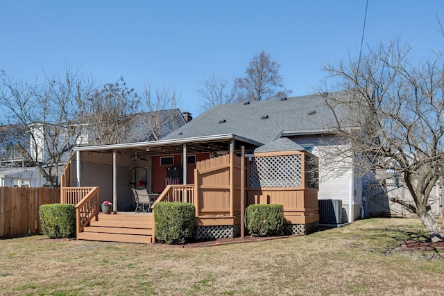 rear view of property featuring roof with shingles, fence, a deck, a yard, and central air condition unit