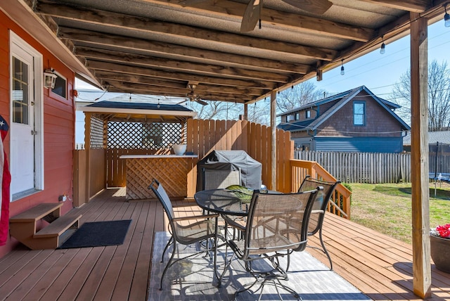 deck featuring a trampoline, fence, a ceiling fan, and outdoor dining space