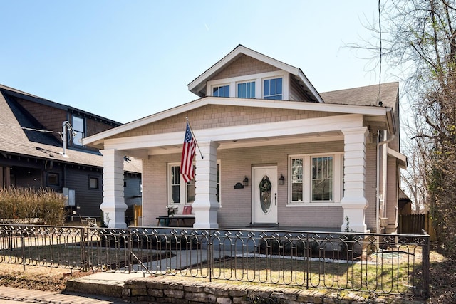 bungalow featuring a fenced front yard, a porch, and brick siding