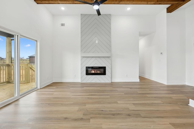 unfurnished living room with light wood finished floors, baseboards, visible vents, beamed ceiling, and a fireplace