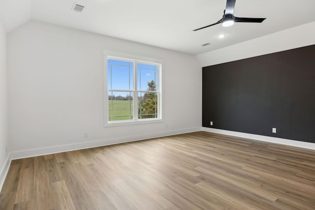 spare room with visible vents, vaulted ceiling, baseboards, and wood finished floors