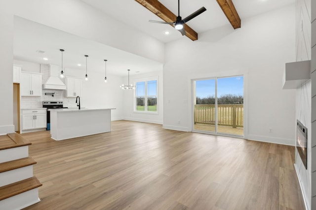 unfurnished living room featuring a sink, light wood-style flooring, beamed ceiling, and ceiling fan with notable chandelier