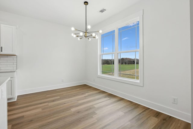 unfurnished dining area featuring light wood finished floors, baseboards, visible vents, and an inviting chandelier