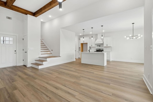 unfurnished living room with light wood finished floors, visible vents, stairway, beamed ceiling, and a sink