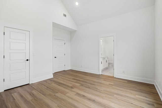 unfurnished bedroom with high vaulted ceiling, visible vents, baseboards, light wood-type flooring, and ensuite bath