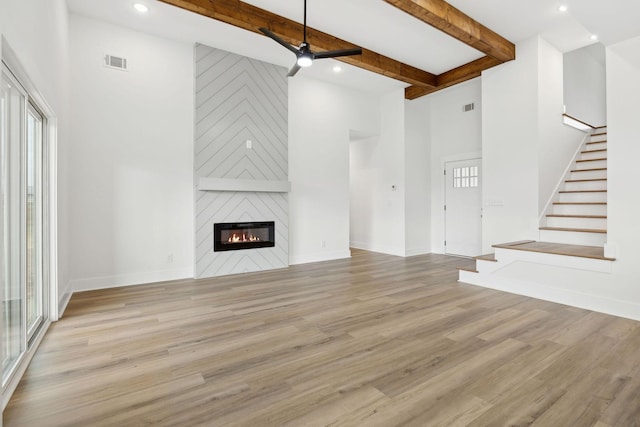 unfurnished living room featuring a large fireplace, baseboards, visible vents, stairway, and wood finished floors