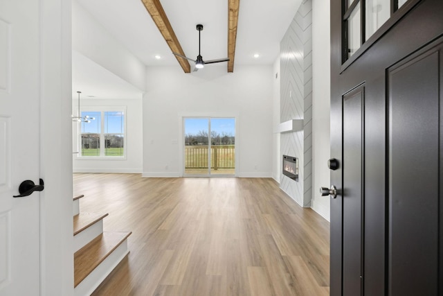 unfurnished living room with plenty of natural light, light wood-style flooring, a fireplace, and beamed ceiling