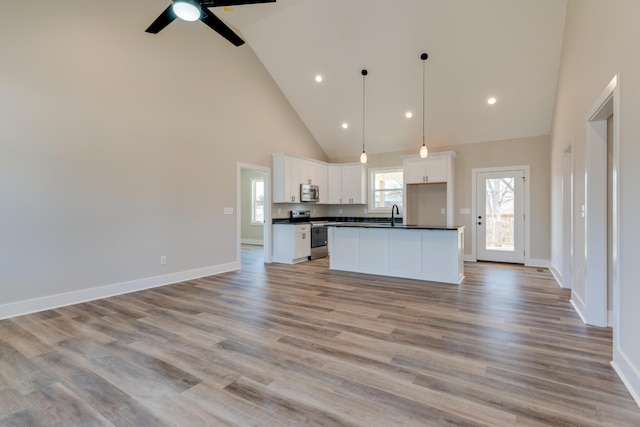 kitchen featuring stainless steel appliances, a sink, open floor plan, light wood finished floors, and dark countertops