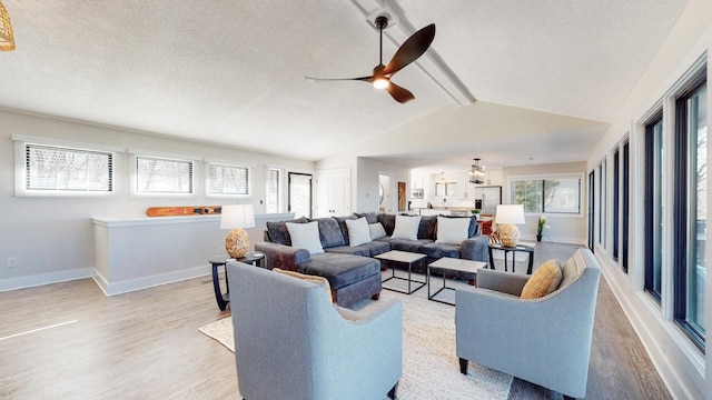 living area with lofted ceiling with beams, a textured ceiling, wood finished floors, a ceiling fan, and baseboards