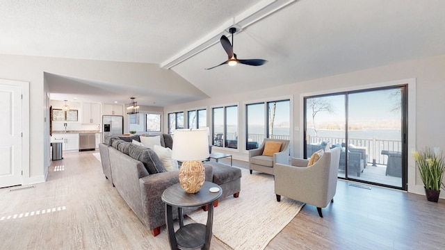 living area featuring lofted ceiling with beams, light wood-type flooring, a ceiling fan, and a healthy amount of sunlight