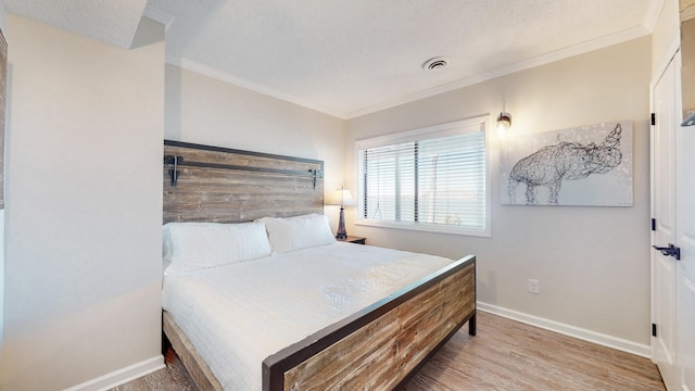 bedroom featuring visible vents, baseboards, wood finished floors, and ornamental molding