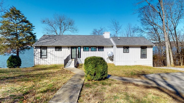 view of front of house featuring a shingled roof, a chimney, and a front lawn