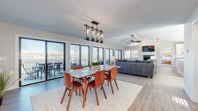 dining space featuring vaulted ceiling, light wood-style flooring, a fireplace, and visible vents