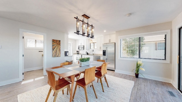 dining room featuring visible vents, light wood-style flooring, baseboards, and an inviting chandelier