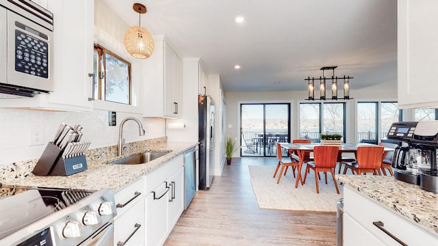 kitchen featuring light wood-style flooring, a sink, stainless steel appliances, white cabinetry, and backsplash