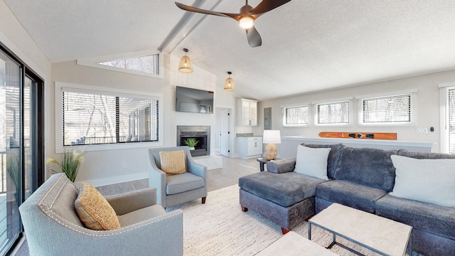 living room with light wood finished floors, baseboards, a fireplace with raised hearth, vaulted ceiling with beams, and a textured ceiling