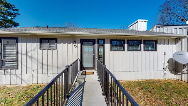 entrance to property featuring a shingled roof, a chimney, and board and batten siding