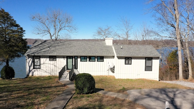 view of front facade with roof with shingles, a chimney, and a front lawn