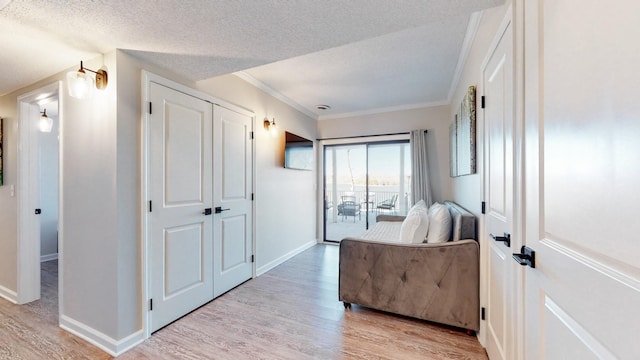 bedroom with ornamental molding, light wood-type flooring, a textured ceiling, and baseboards