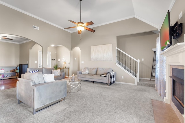 living room with visible vents, a fireplace with flush hearth, a ceiling fan, arched walkways, and crown molding