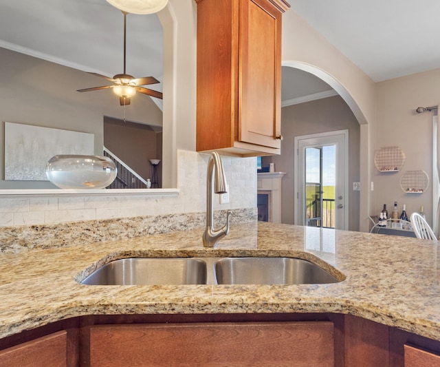 kitchen with a sink, decorative backsplash, light stone counters, and brown cabinetry