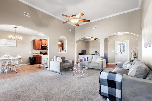 living room with visible vents, ceiling fan with notable chandelier, arched walkways, crown molding, and light colored carpet