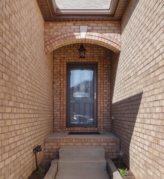 view of exterior entry with brick siding and a shingled roof