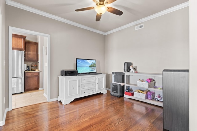 rec room with a ceiling fan, wood finished floors, visible vents, and ornamental molding