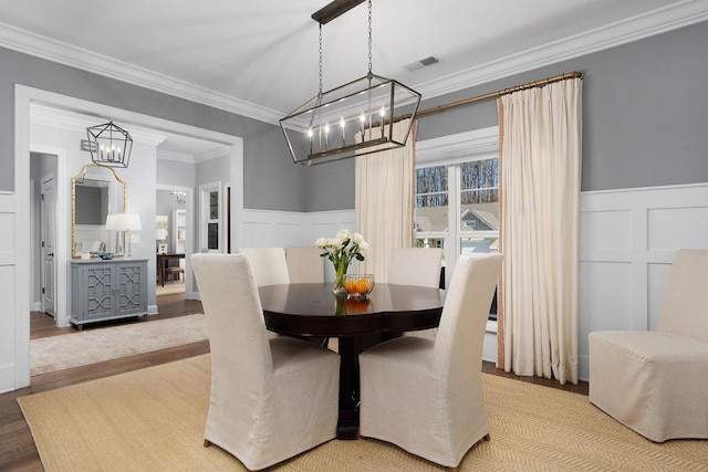 dining area with a wainscoted wall, ornamental molding, wood finished floors, and visible vents