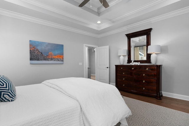 bedroom with wood finished floors, a ceiling fan, baseboards, ornamental molding, and a tray ceiling