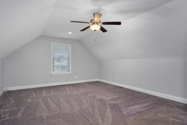 additional living space featuring visible vents, baseboards, ceiling fan, vaulted ceiling, and dark colored carpet