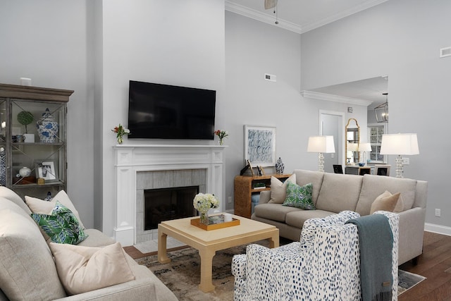 living area featuring visible vents, a tiled fireplace, a towering ceiling, wood finished floors, and crown molding