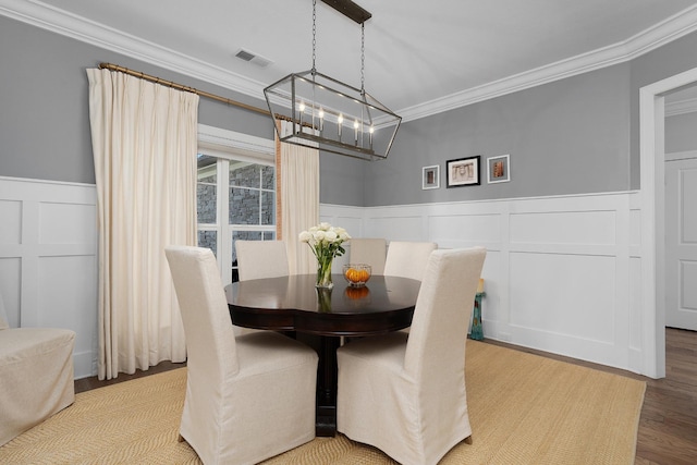 dining room with a notable chandelier, a wainscoted wall, wood finished floors, visible vents, and crown molding