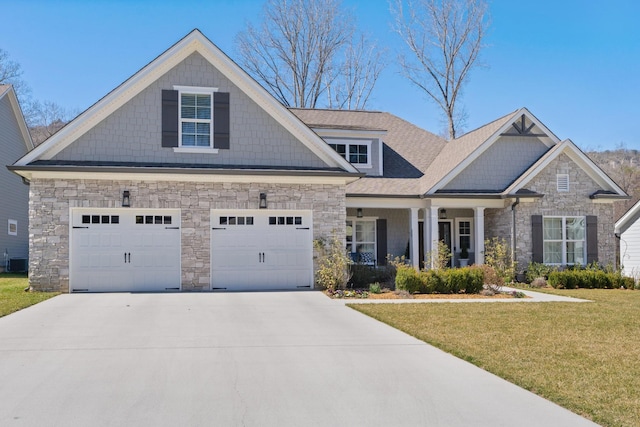 craftsman-style house with covered porch, concrete driveway, stone siding, and a front yard