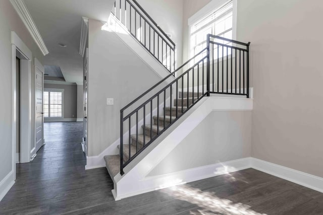 staircase featuring wood finished floors, a towering ceiling, and baseboards