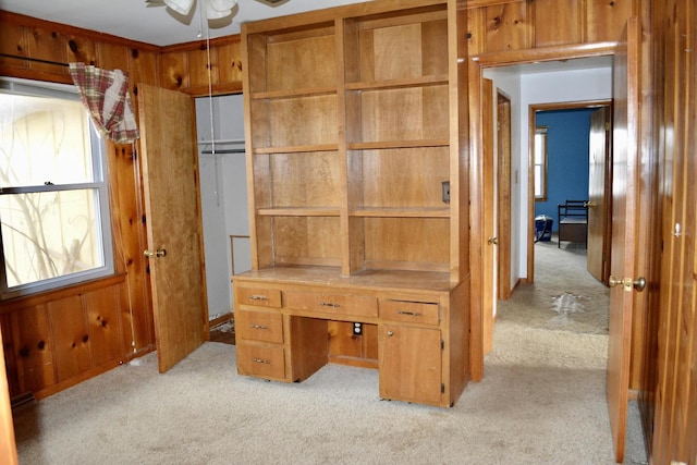 unfurnished office featuring wood walls, a ceiling fan, and light colored carpet